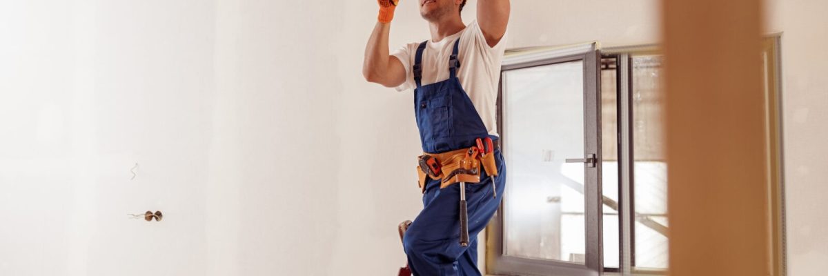 Smiling electrician fixing electric cable on ceiling
